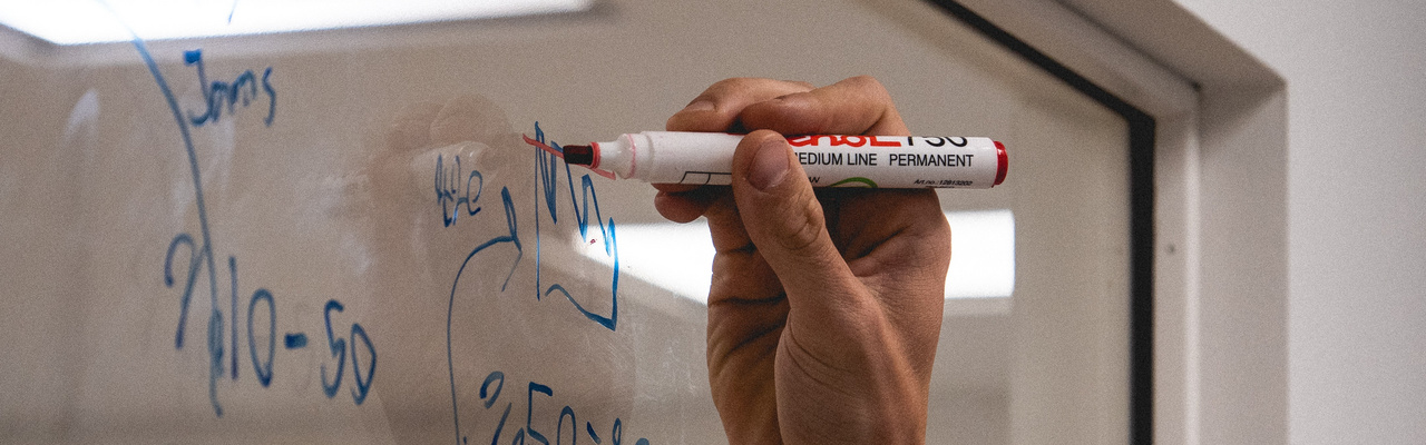 Titelbild Prozessmanagement Eine Hand malt mit einem Stift etwas an eine Glasscheibe.